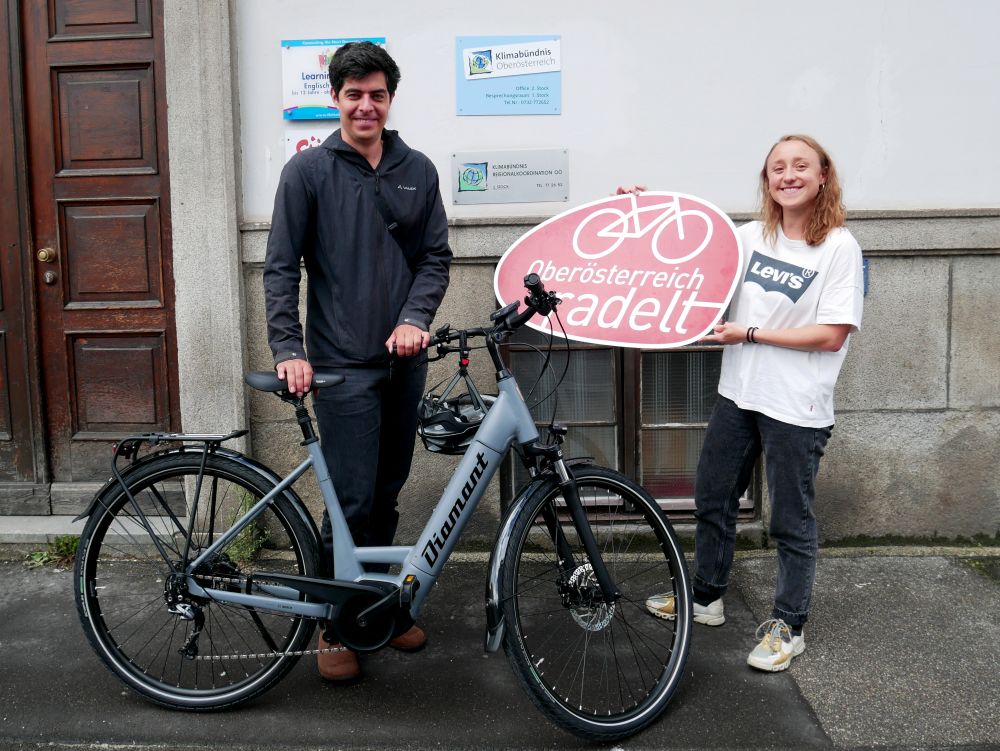 Gewinner des Radel-Lottos mit E-Bike und junge Frau mit Oberösterreich radelt Schild.
