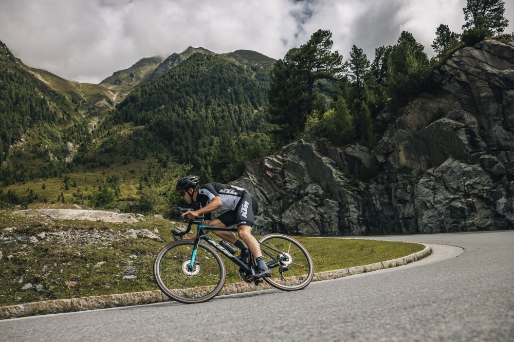 Fahrradfahrer fährt bergab auf einer Strecke, im Hintergrund ist eine Berglandschaft