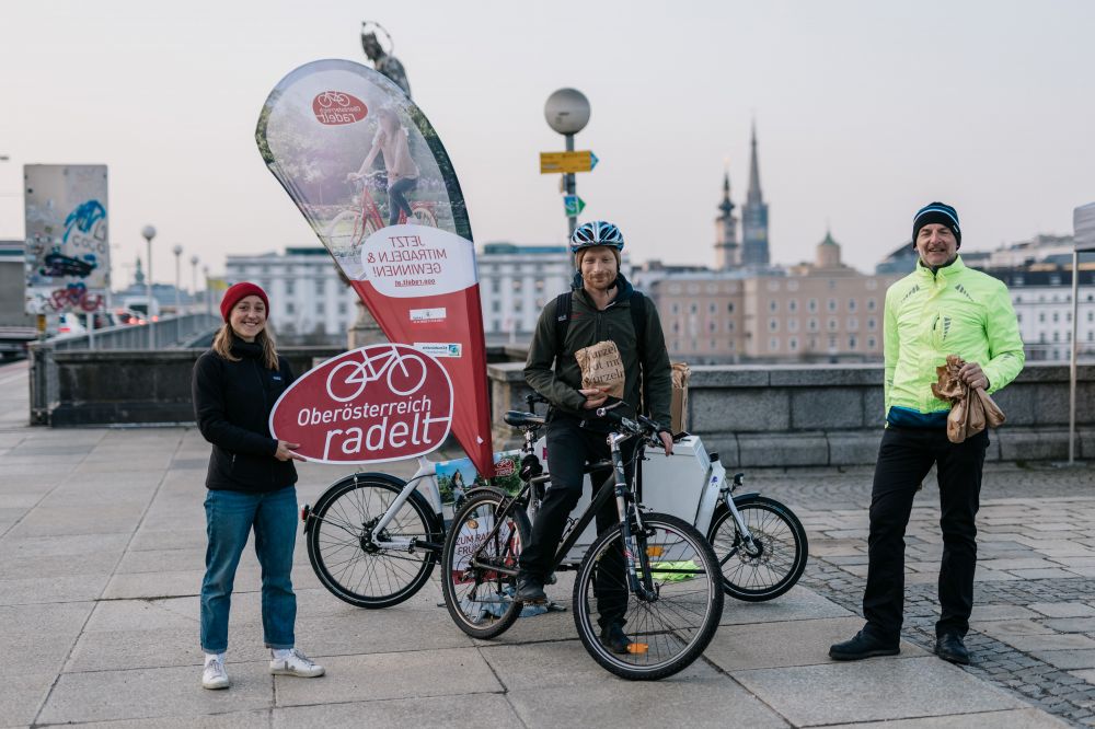 Drei Personen, davon eine am Fahrrad mit Frühstück in der Hand.