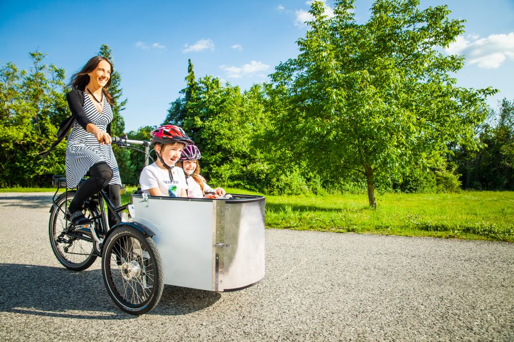 Frau auf Lastenrad mit zwei Kindern vorne im Fahrrad