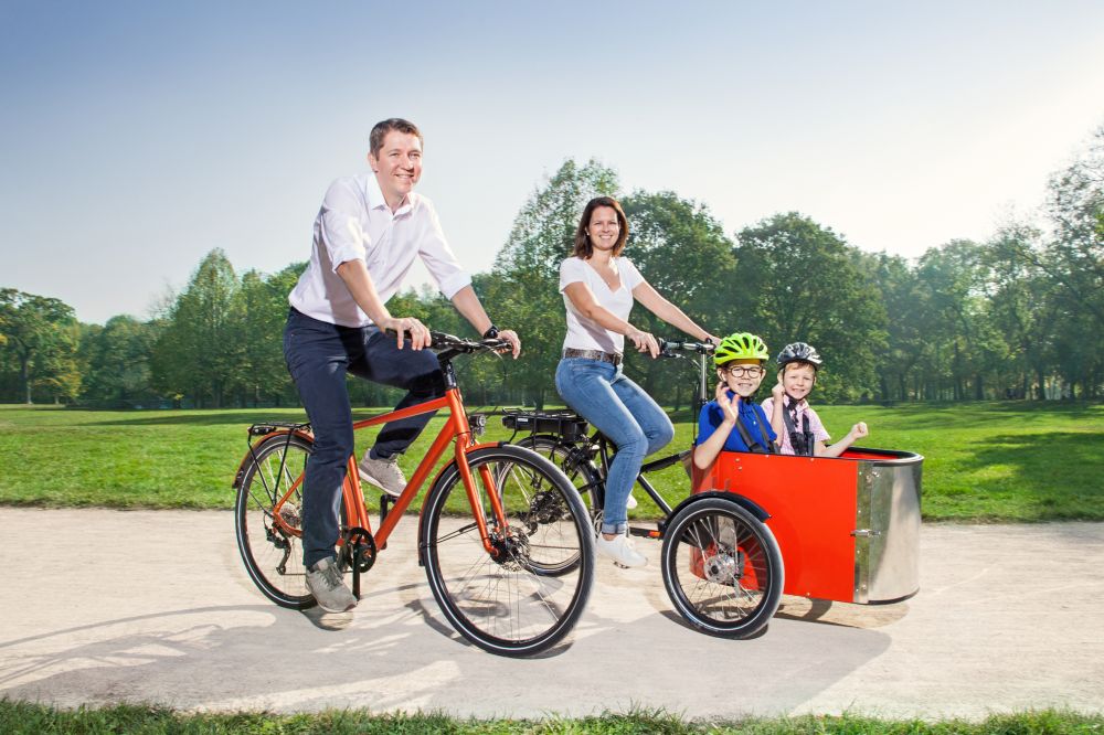 Familie auf zwei Fahrrädern im Park. Kinder sitzen im Lastenrad.